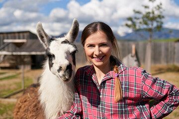 Young woman in shirt standing next to white llama at zoo on a sunny day, smiling, posing for picture © Lubo Ivanko