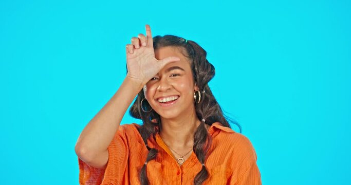 Woman, laughing and loser sign on face with pointing for joke, bullying or funny by blue background. Gen z girl, hand gesture and comic portrait with laugh, playing or emoji for happiness in studio
