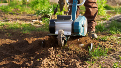 A farmer is digging up a vegetable garden with an electric cultivator.