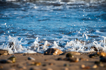 Selective focus on the sand and stones of a beach with the sea breaker in the background.