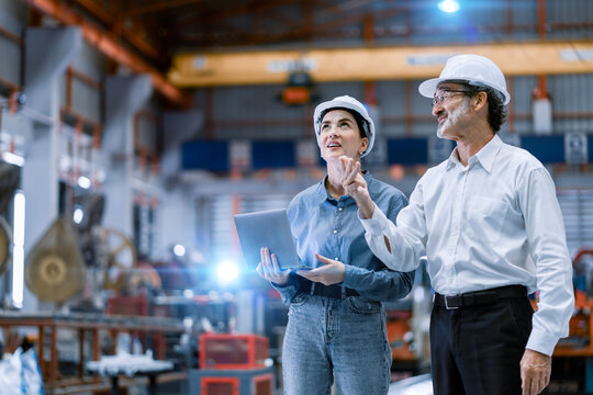 professional engineer,worker,technician use clipboard discuss work, walk in steel metal manufacture factory plant industry. Black African American man and woman wear hard hat check quality machine.