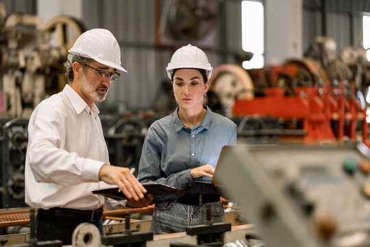 professional engineer,worker,technician use clipboard discuss work, walk in steel metal manufacture factory plant industry. Black African American man and woman wear hard hat check quality machine