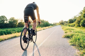 Foto op Plexiglas Rear view of a cycling man riding a bike outside during a sunset © Zamrznuti tonovi