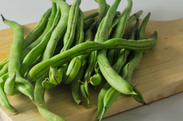 Some green beans on a wooden cutting board isolated on a white background