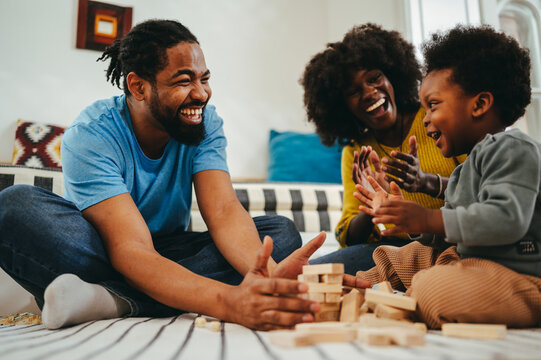 Happy african american parents are clapping and smiling at their cute son during playtime at home.
