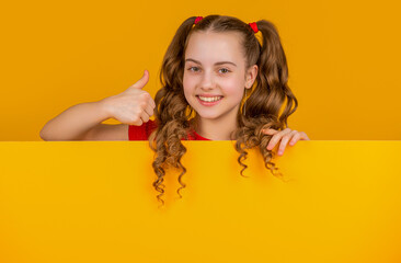 cheerful kid behind blank yellow paper with copy space for advertisement. thumb up