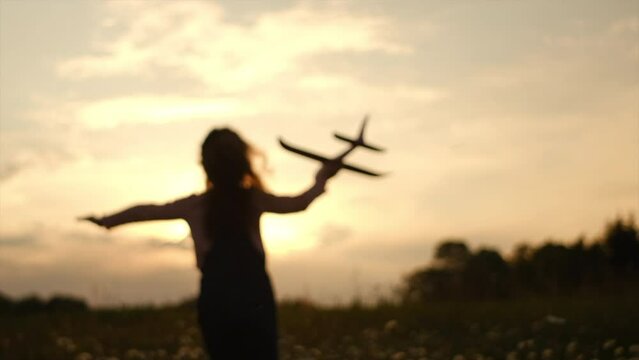 Silhouette of playful little girl run with an airplane on background amazing summer sunset and epic mountains. Dream freedom concept. Child runs on field holding in hands toy aircraft. Selective focus