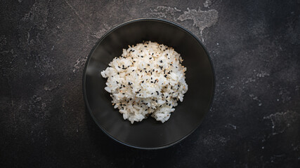 Obraz na płótnie Canvas Boiled rice with sesame seeds in a black plate on a black background. View from above