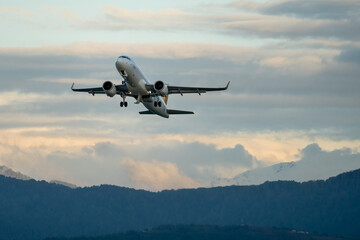 Passenger airplane after takeoff against backdrop of mountains and sunset cloudy sky on background....
