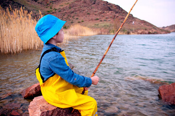 a little fisherman boy with a fishing rod in a yellow fishing jumpsuit