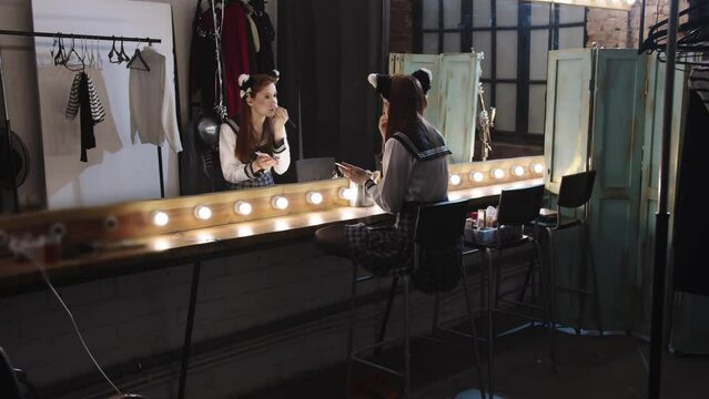 Cute woman cosplayer in school uniform doing makeup at the backstage mirror