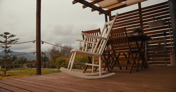 Empty rocking chair swings in wind on backyard in cloudy day, melancholic lonely mood