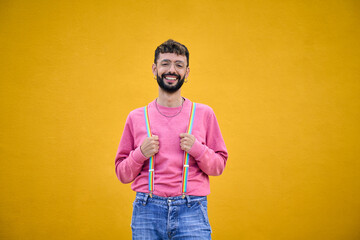 Smiling cheerful young Caucasian man holding his rainbow lgbt suspenders. Gay people posing for...