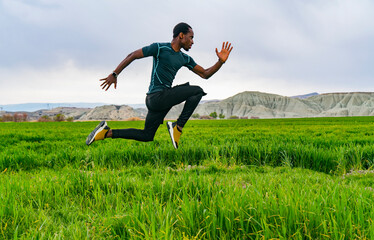 Fototapeta na wymiar Man running in nature. Black young male athlete goes running outdoors. athlete jumping high while running in nature