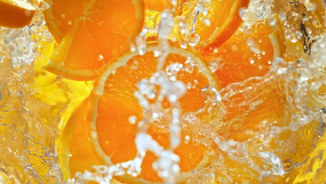 Super Slow Motion Shot of Fresh Orange Slices Falling into Water Whirl at 1000 fps.