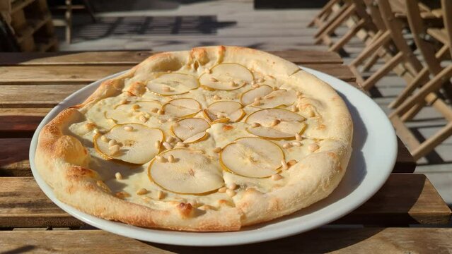 pear and cheese pizza on a white plate in a street cafe stands on a wooden table