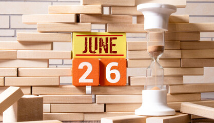 Calendar for June 26, made wooden cubes, against light concrete wall.With an empty space for your text