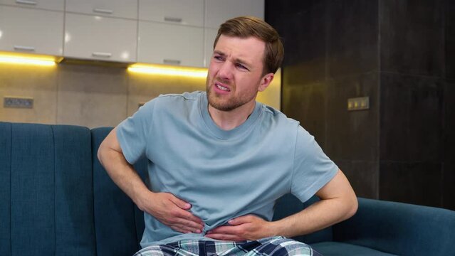 Young man suffering stomach ache sitting on a couch in the living room at home
