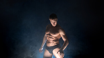 Muscular athlete in an epic pose, dark background, bright light from below, the concept of sports and bodybuilding