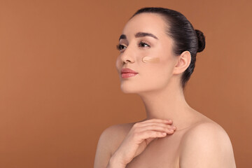 Woman with swatch of foundation on face against brown background. Space for text