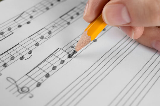 Woman writing musical notes with pencil on sheet of paper, closeup