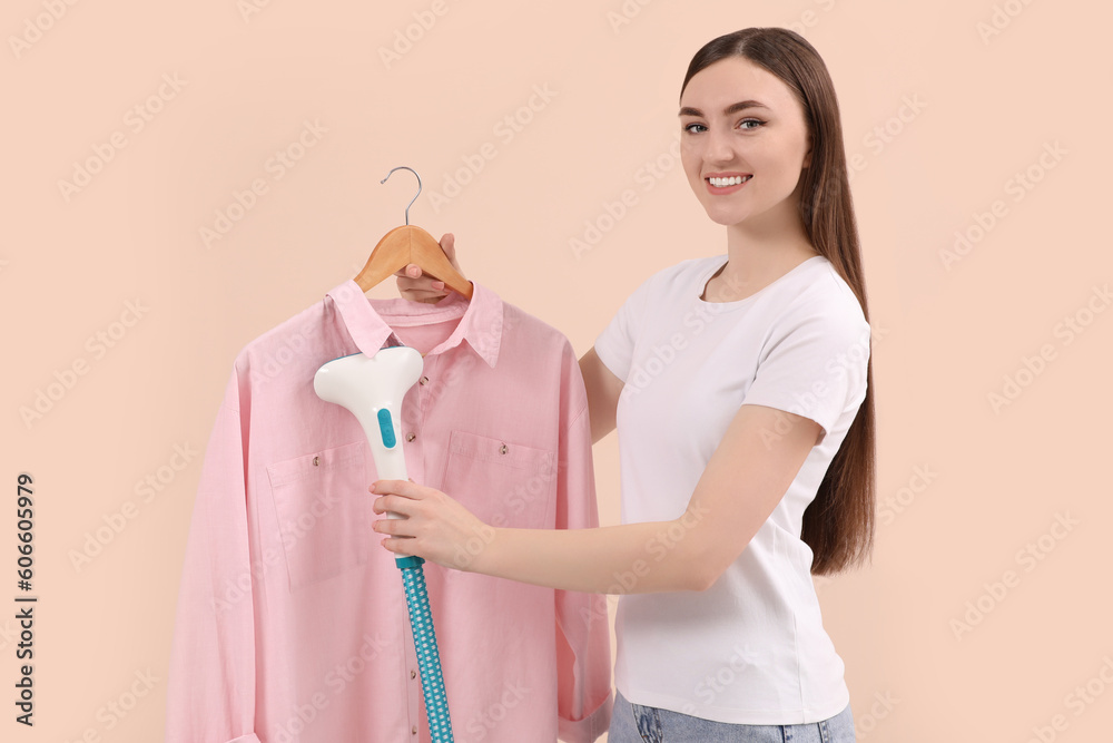 Wall mural Woman steaming shirt on hanger against beige background