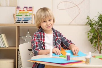 Fototapeta na wymiar Cute little boy with colorful paper at desk in room. Home workplace