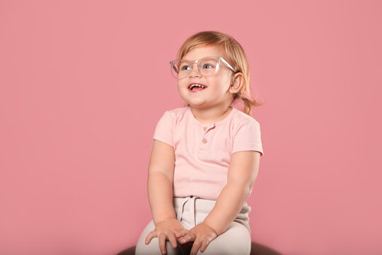 Cute little girl in glasses on pink background. Space for text