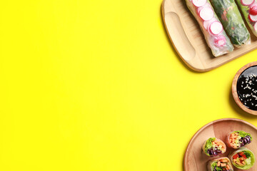 Different delicious spring rolls and soy sauce on yellow background, flat lay. Space for text