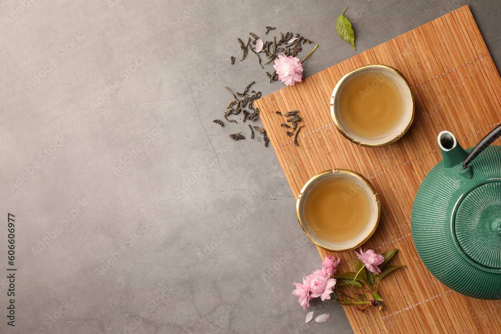 Poster Traditional ceremony. Cups of brewed tea, teapot and sakura flowers on grey table, flat lay with space for text