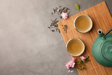 Traditional ceremony. Cups of brewed tea, teapot and sakura flowers on grey table, flat lay with space for text - obrazy, fototapety, plakaty