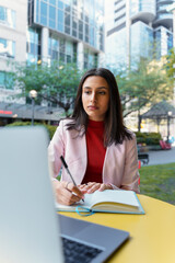 Serious smart asian student studying, learning language in university campus. Young pensive Indian businesswoman, freelancer using laptop, taking notes, planning project working online at workplace