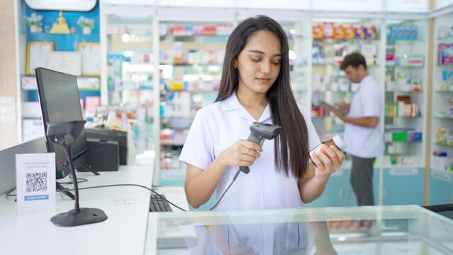 Medical pharmacy and healthcare business concept. Indian woman pharmacist checking medical product, medicine and supplements in stock by scan barcode on package at cashier counter in modern drugstore.