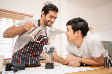 Cheerful Boyfriends gay LGBTQ lovely couple making a drip coffee brew in the kitchen together for...