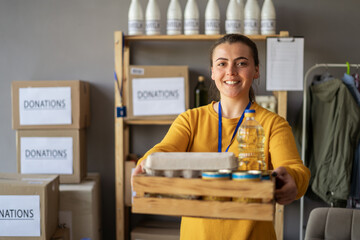 Portrait of happy smiling female volunteer with food in box at distribution or refugee assistance center. Charity, donation and volunteering concept - obrazy, fototapety, plakaty
