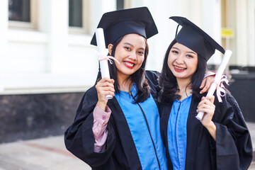 Two Asian women university graduates celebrate with happiness with friends after receiving...