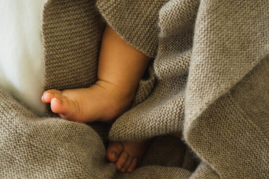 Close-up of Latino Baby Feet Covered with Brown Cashmere Blanket on a White Cotton Duvet