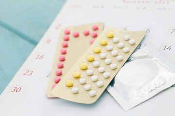 Contraceptive control pills and condom on date of calendar background  calculate date Control the birth rate. health care and medicine, contraception concept. empty space for text.