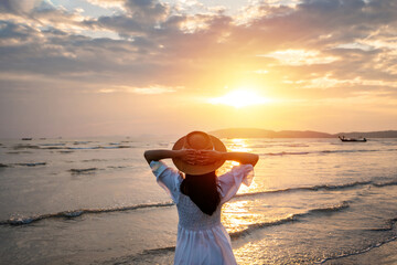 Young woman traveler relaxing and enjoying the beautiful sunset on the tranquil beach, Travel on...