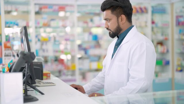 Medical pharmacy and healthcare providers concept. Handsome Indian man pharmacist working inspection medical product, drugs, medicine and supplements in package at cashier counter in modern drugstore.