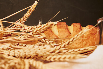 a loaf of bread on burlap, coarse flour, grains and ears of wheat
