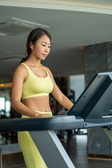 Attractive young running sports woman is working out in gym. Doing cardio training on treadmill. Running on treadmill. Young girl spending time fitness room on roof top of condominium