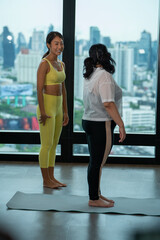 Fototapeta na wymiar Fitness instructor trains fat woman stretching Yoga meditates against modern skyscrapers room on roof top of Condominium.