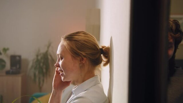Woman talks by phone. Man smiles, overhears the conversation in the neighbor room or apartment through the wall using cup. Apartment with thin walls, without sound insulation. Concept of neighborhood.