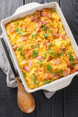 Traditional baked Austrian Schinkenfleckerl with Fleckerl pasta, ham, sour cream, eggs and breadcrumbs closeup on the baking dish on the table. Vertical top view from above