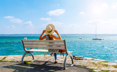 Woman sitting on a bench looking at atlantic ocean and boats- vacation, travel destination, relaxing, summer holiday ( Le croisic in France, Loire atlantic) - obrazy, fototapety, plakaty