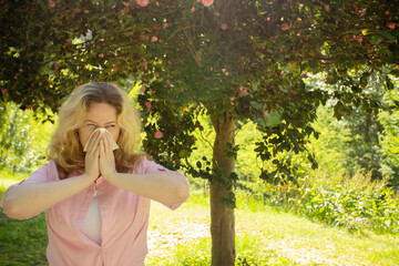 Seasonal allergies, Runny nose, Watery eyes, woman allergic sneezes under a tree with flowers in the park