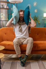 Repair work at neighbours. Irritated young man relaxing on couch cover ears with pillows annoyed by...