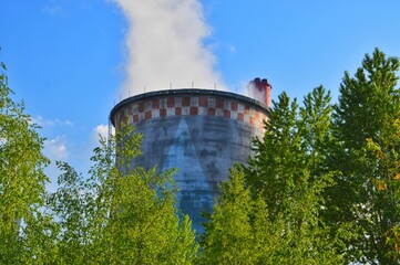 A thick colored pipe at a nuclear power plant evaporates excess water into the blue sky.