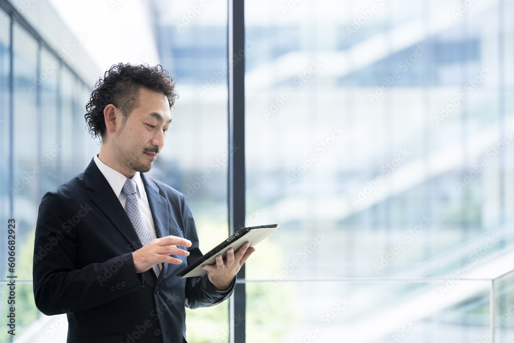 Wall mural Handsome Asian businessman checking his tablet in his beautiful office.thinking